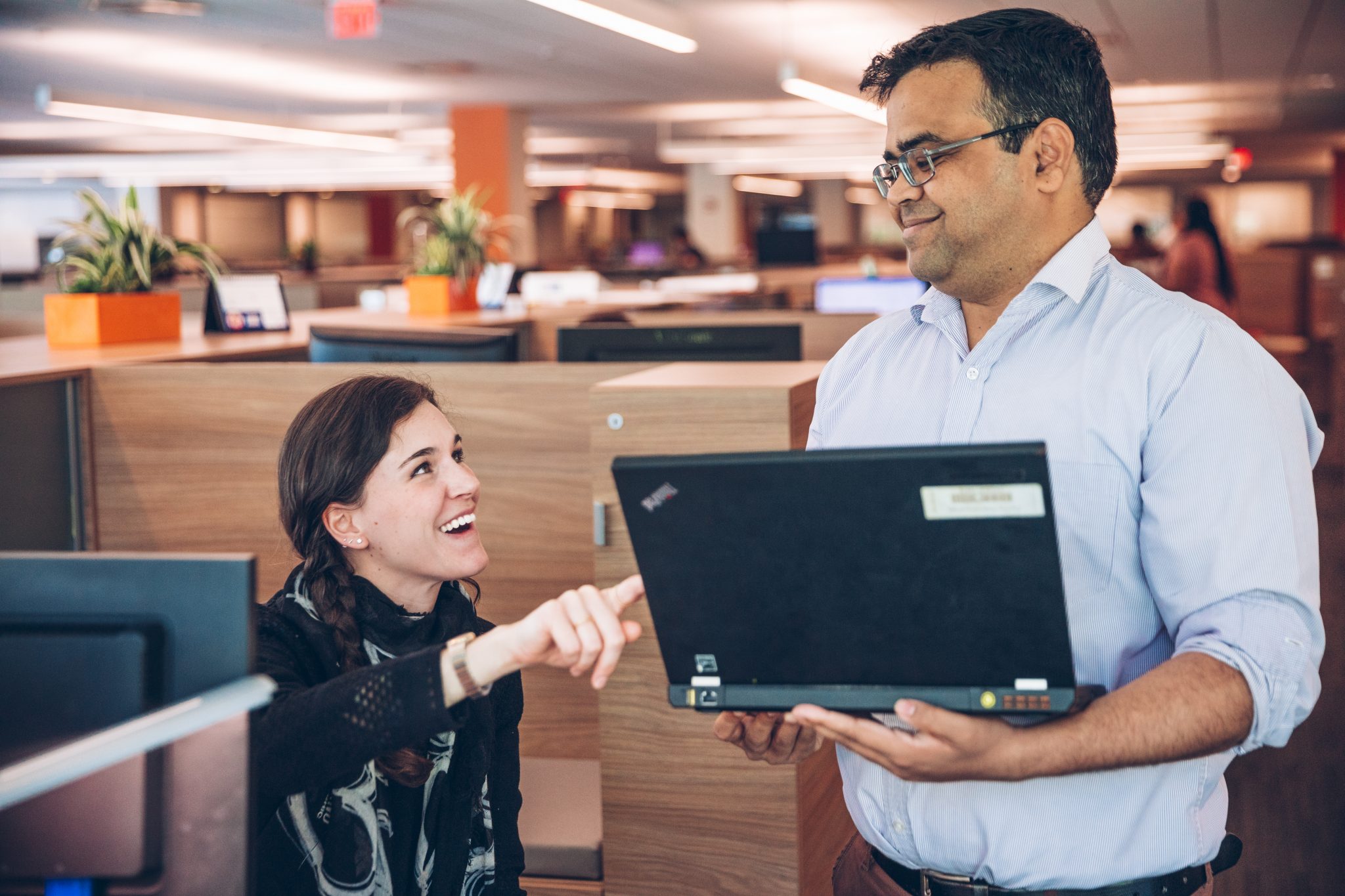 A seated women points at a standing colleagues computer and smiles