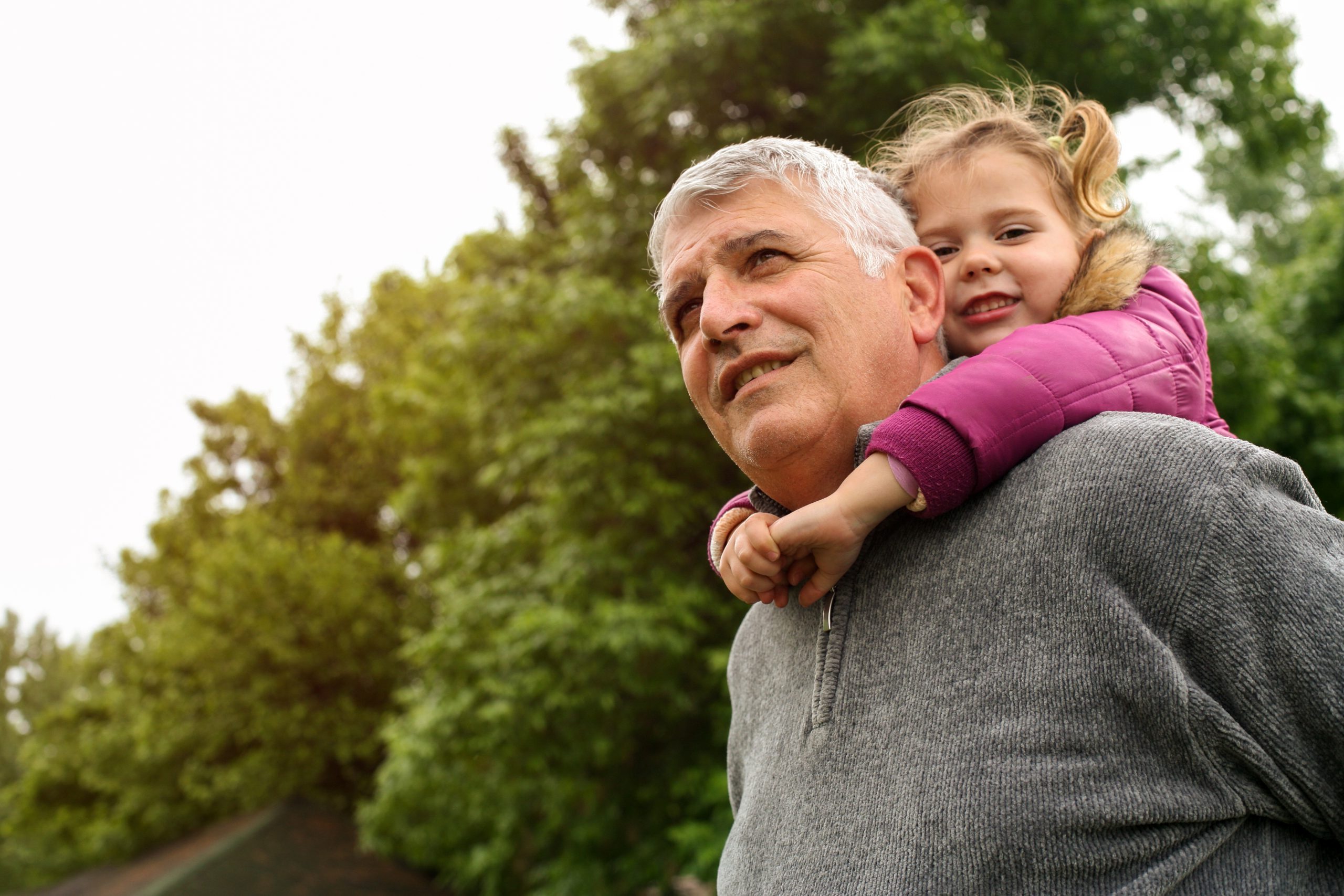 Grandfather with his granddaughter in the park. Little girl looking at camera.