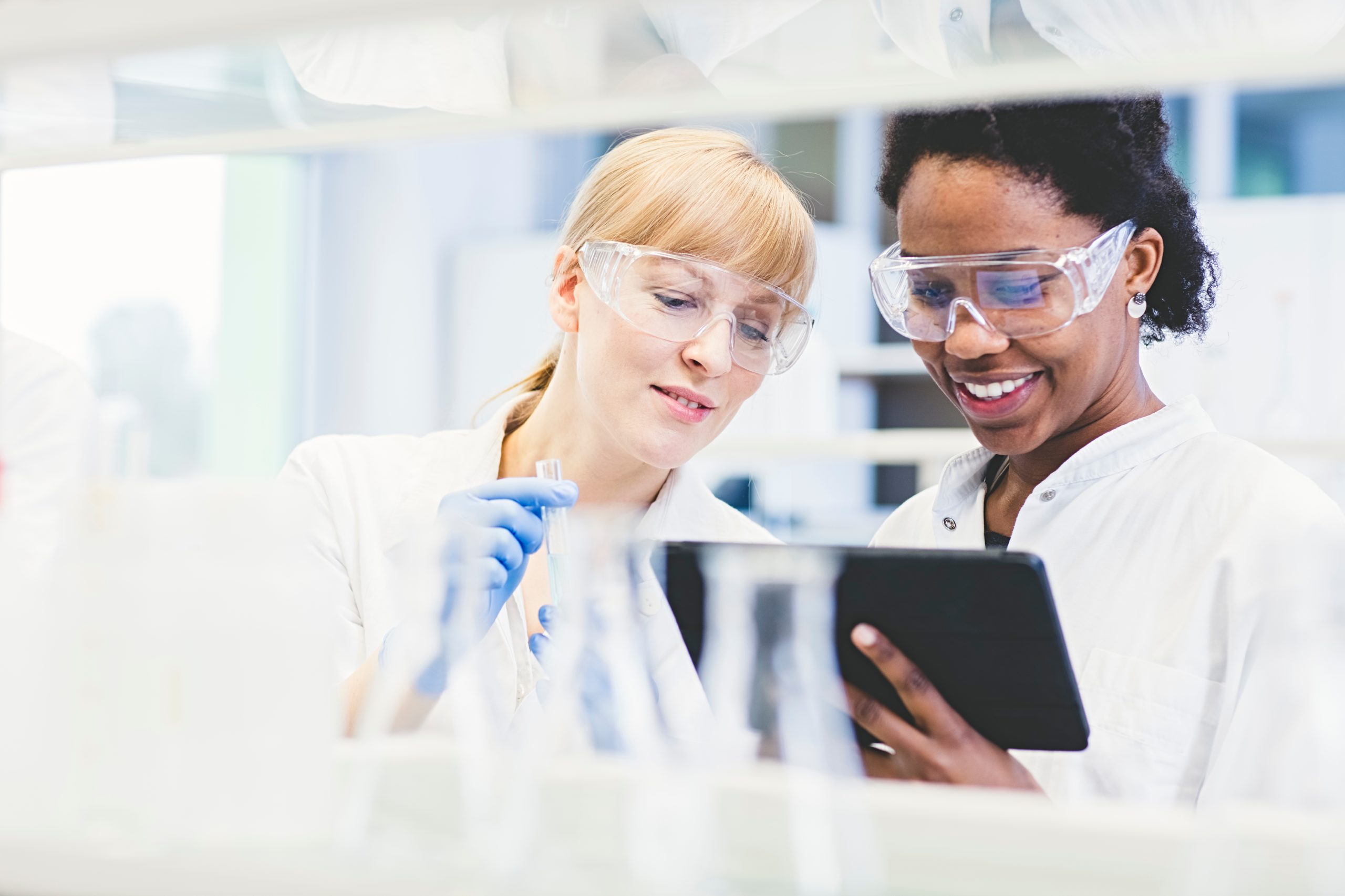 Two smiling female scientists in a lab observing a tablet