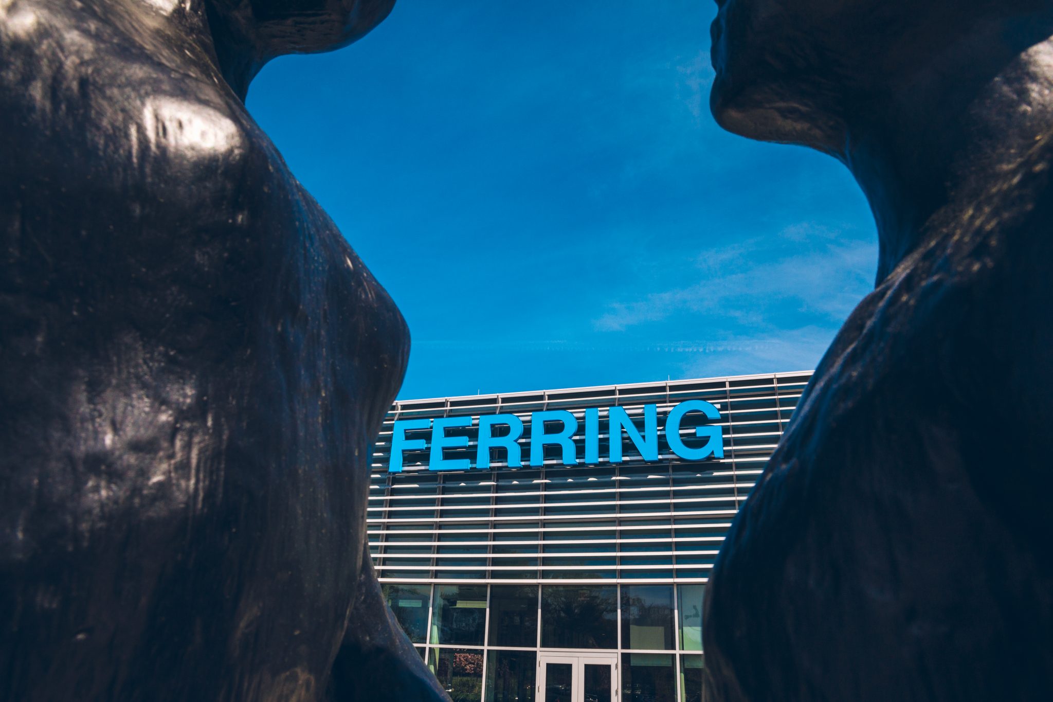 The Ferring logo on a building as seen from a distance framed between two statues in the foreground