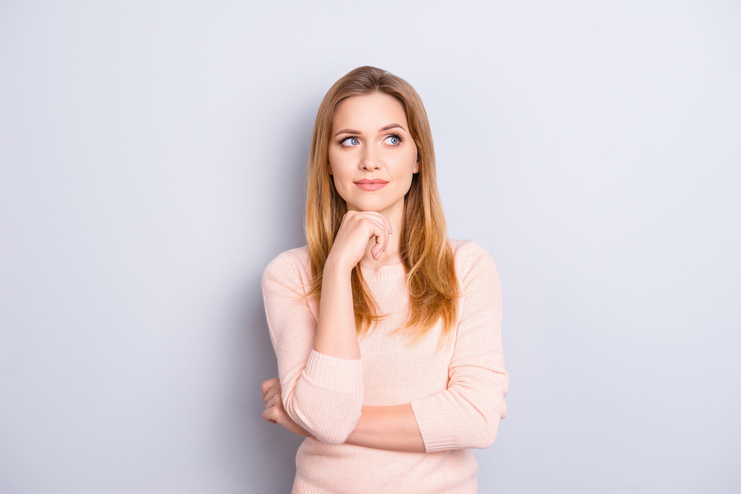 A woman stands alone, arms folded, pondering against a white wall