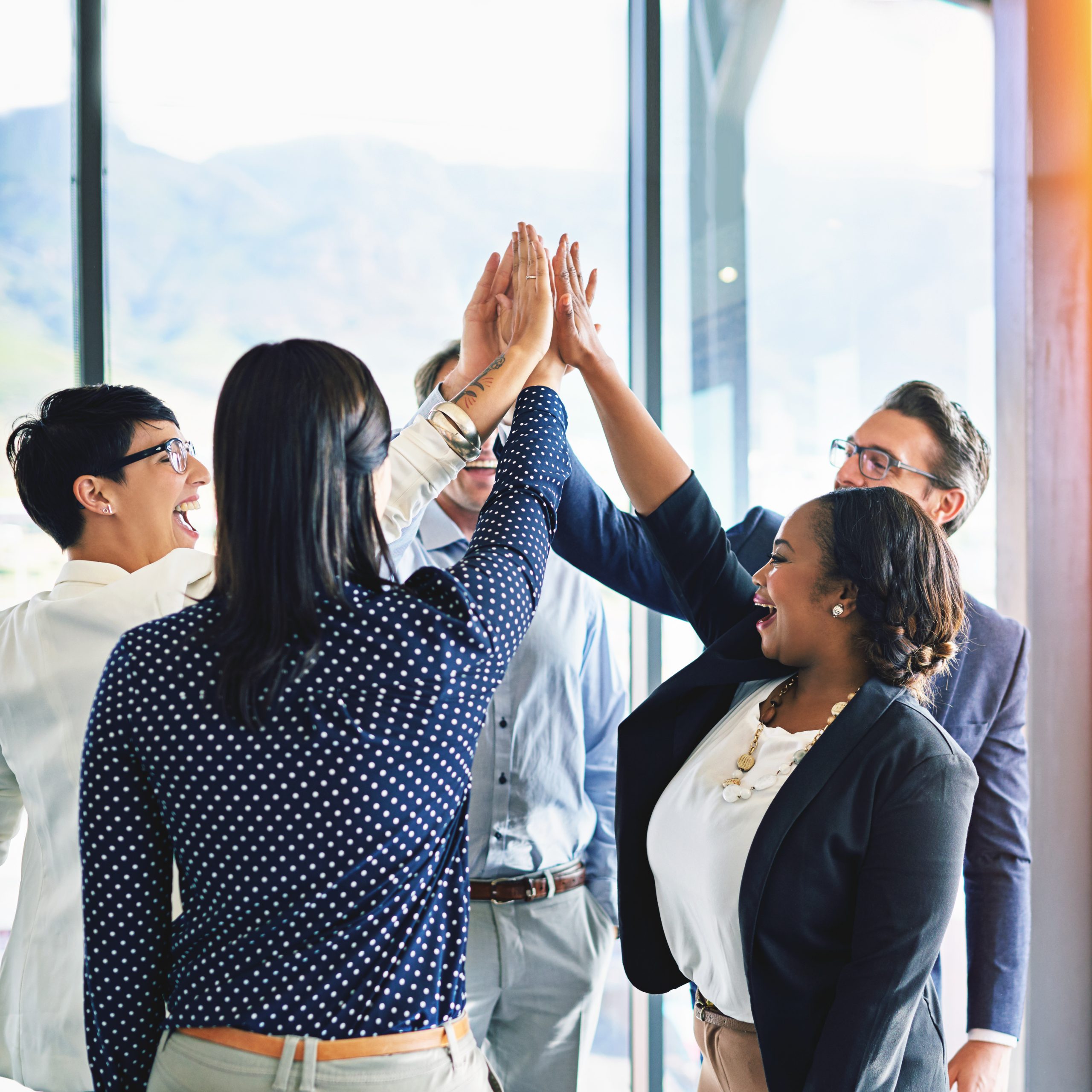 Five co-workers, 2 women and 3 male, raise hands together in symbol of teamwork