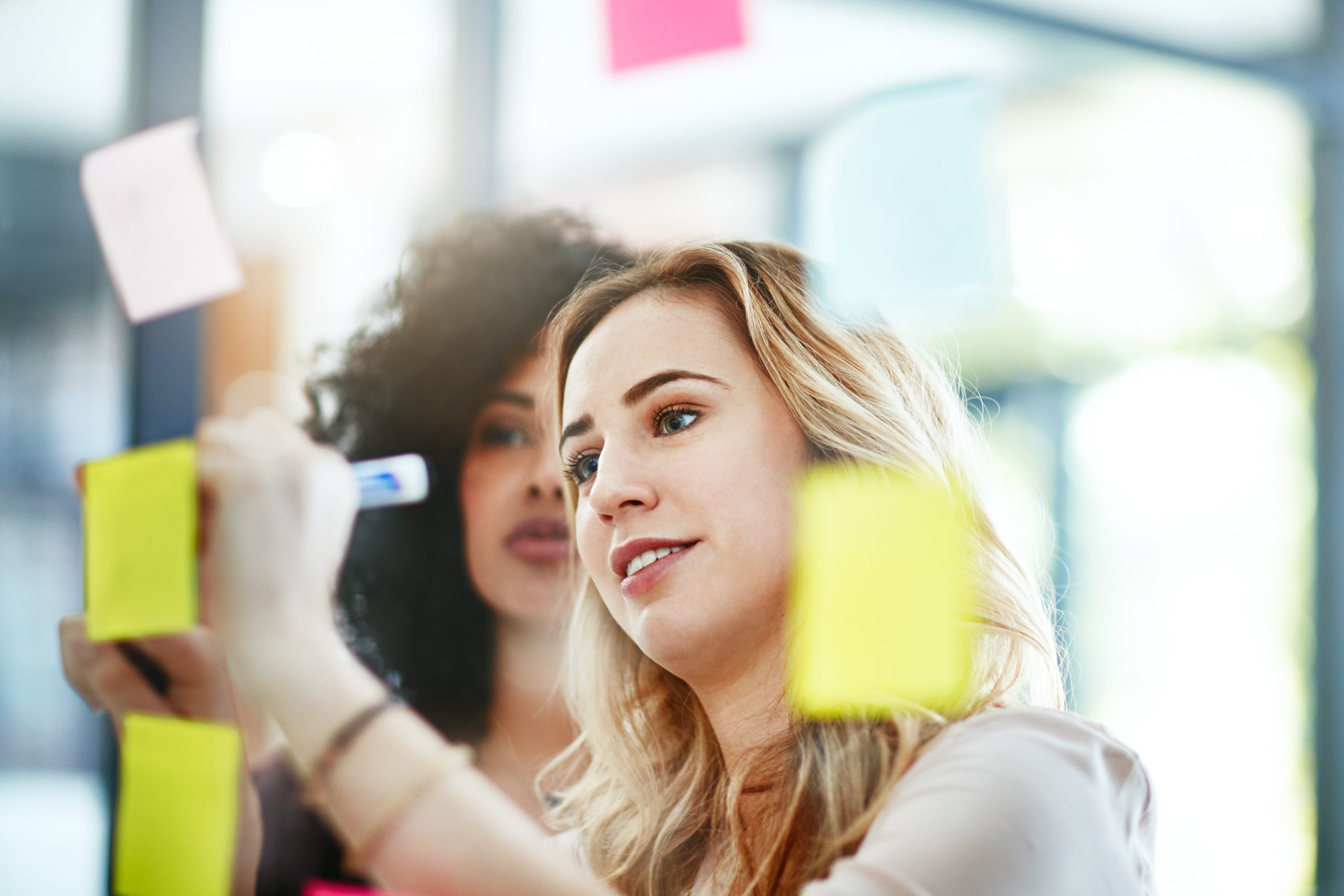 Two women collaborating, posting notes on glass