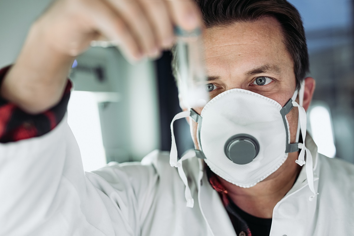 A man wearing a mast examines a sample in a lab